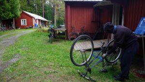 Bike being fixed on grass. Red wooden houses at the back.